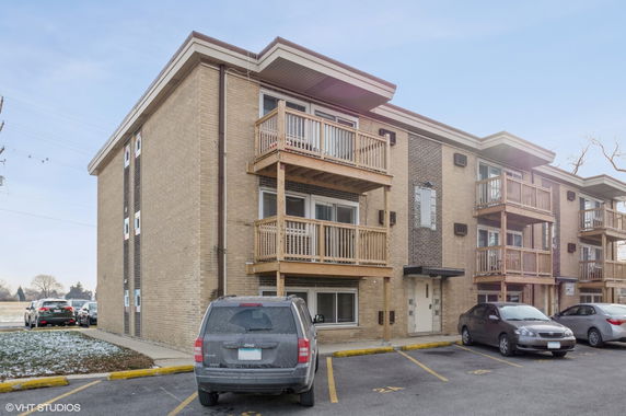 Front view of a multi-story building with balconies and parking area.