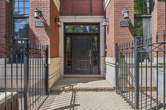 Front view of a brick building entrance with brown door and black iron fence.
