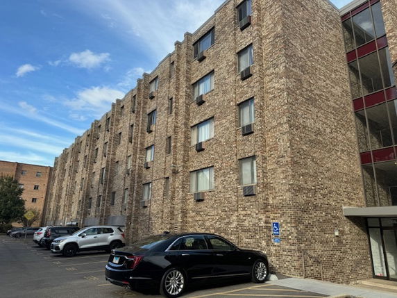 Front view of a multi-story brick building with several windows and a parking area in front.