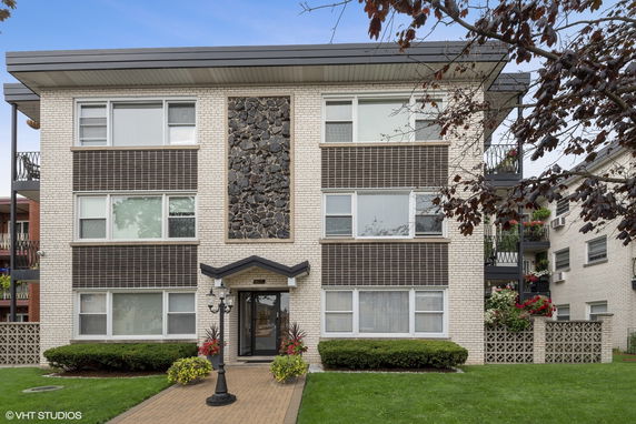 Front view of a three-story apartment building with a brick exterior and central stone accent.