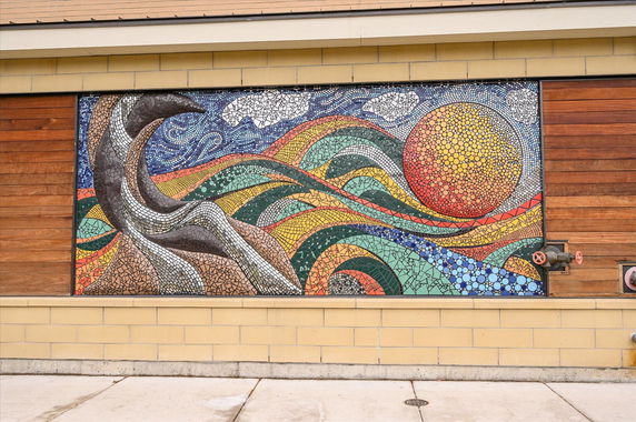 Front view of a building with a colorful mosaic mural featuring abstract designs and a large sun.