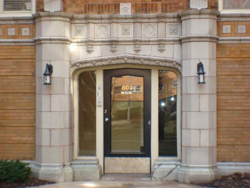 Front view of a decorative entrance to a building with an arched doorway and wall sconces.