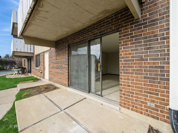 Front view of a multi-story building with a brick exterior and sliding glass doors leading to a small patio.