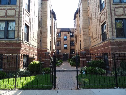 Front view of an apartment building with a gated entrance and landscaped pathway.