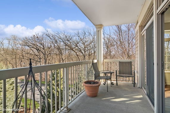 Balcony with chairs overlooking trees and a clear sky.