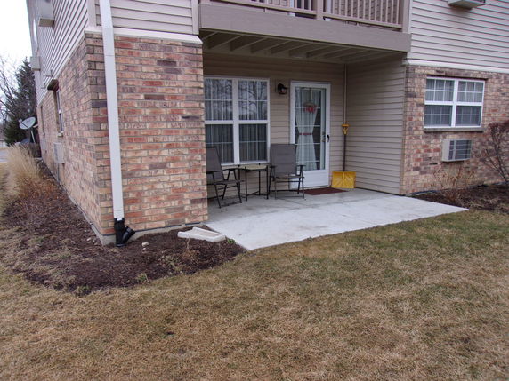 Front view of a brick building corner with a small patio area and chairs.