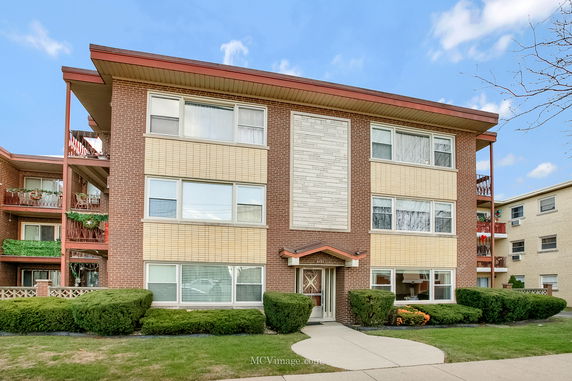 Front view of a three-story apartment building with a mix of brick and siding exterior.