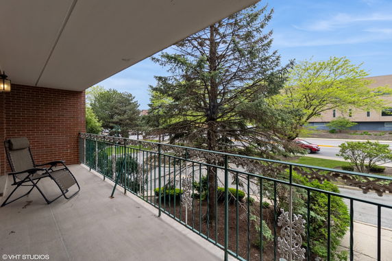 Balcony view overlooking a street with trees and a building in the distance.