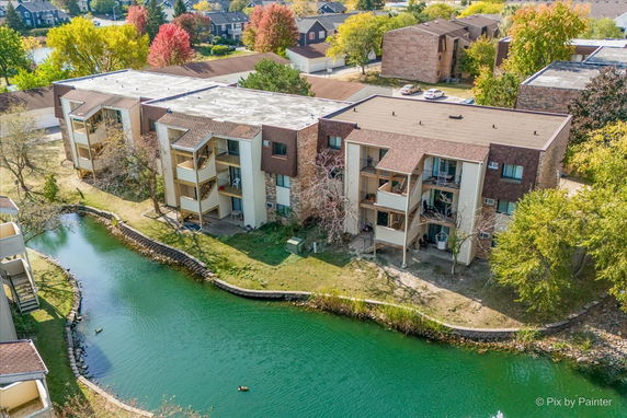 Aerial view of a multi-story apartment building with multiple balconies, situated near a small pond.