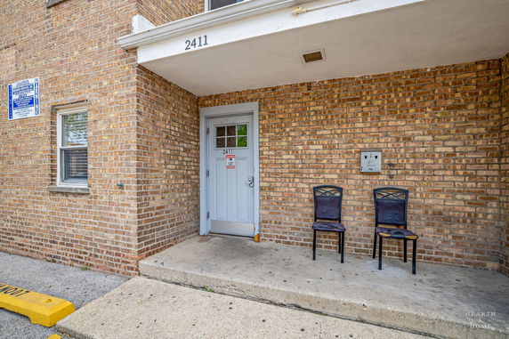 Front view of a brick building entrance with two chairs.