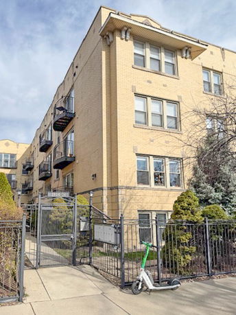 Front view of a multi-story brick apartment building with balconies and a gated entrance.