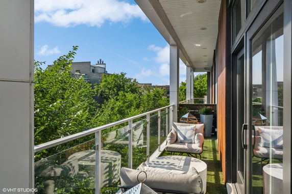 View from a modern building's balcony with outdoor seating overlooking trees and rooftops.