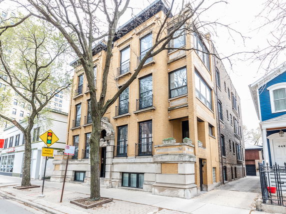 Front view of a multi-story apartment building with large windows and a distinctive stone arch entrance.