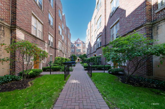 Front view of a multi-story brick residential building with a central pathway leading to an entrance.