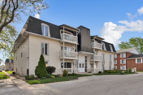 Front view of a multi-story residential building with balconies and a sloped roof.