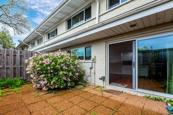 View of the rear side of a two-story building with sliding glass doors and flowering shrubs.