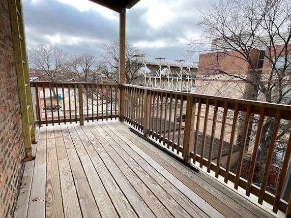 Wooden balcony with railing overlooking urban buildings and trees.