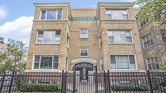 Front view of a three-story brick apartment building with large windows and a gated entrance.