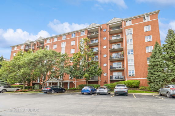 Front view of a multi-story brick apartment building with balconies and parking area.