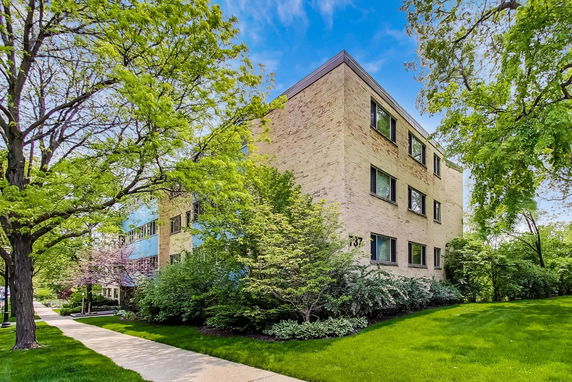 Front view of a three-story brick building with surrounding greenery.