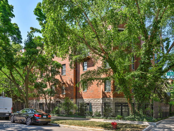 Front view of a multi-story brick apartment building with trees in front.