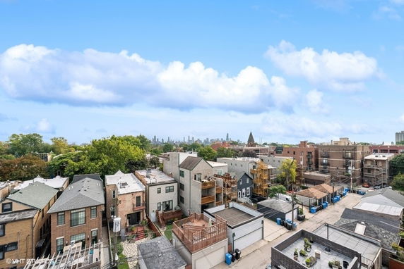 Panoramic view of a neighborhood with residential buildings and trees, city skyline in the background.