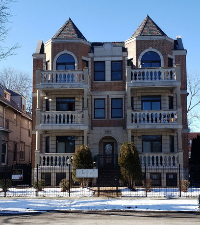 Front view of a multi-story brick apartment building with balconies and triangular roof sections.