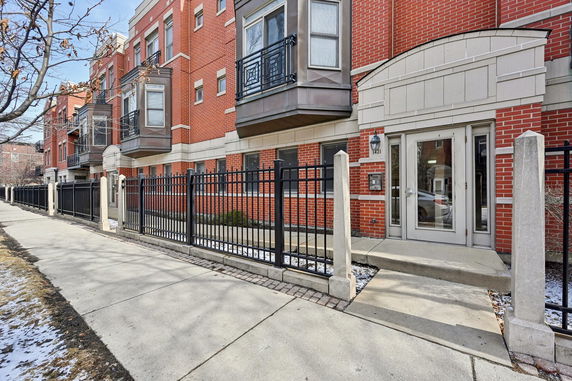 Front view of a multi-story brick building with balconies and a gated entrance.