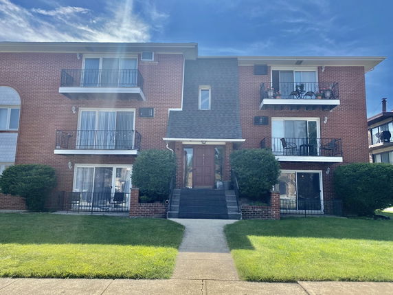 Front view of a three-story brick apartment building with balconies.