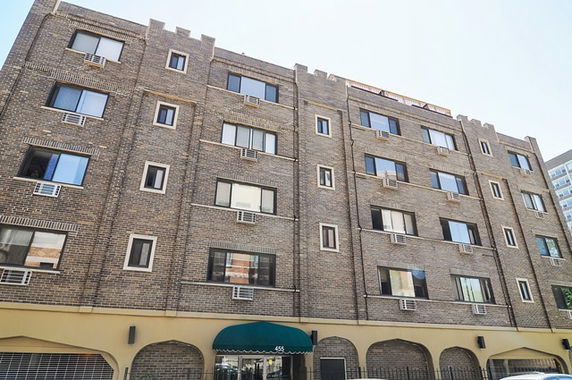 Front view of a multi-story brick apartment building with multiple windows and air conditioning units.