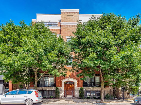 Front view of a multi-story brick building with trees and parked cars along the street.