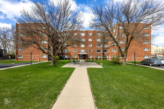 Front view of a multi-story brick apartment building with a path leading to the entrance.