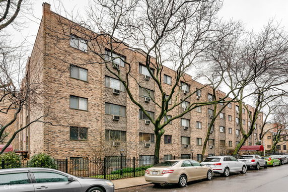 Front view of a multi-story brick apartment building with multiple windows and several parked cars in front.