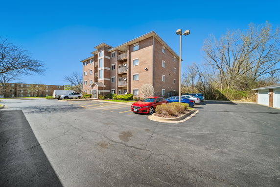 Front view of a four-story brick apartment building with parking area.