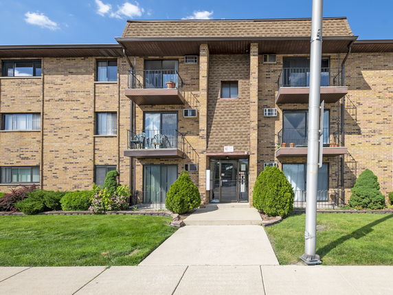 Front view of a multi-story brick apartment building with balconies.