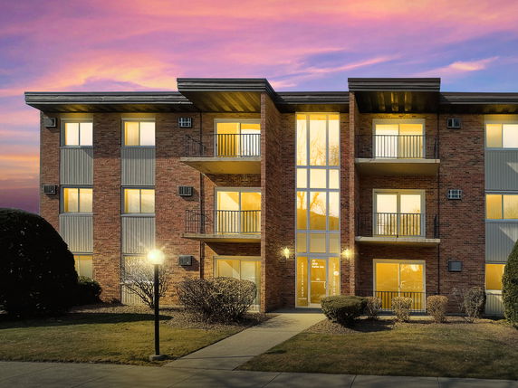 Front view of a three-story apartment building with balconies and large windows.