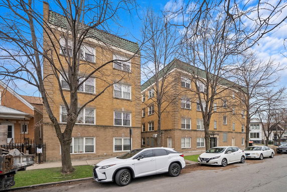 Front view of two adjacent multi-story brick apartment buildings with green roof accents.