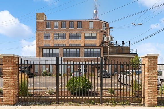 Front view of a multi-story industrial style building with large windows and parking area.