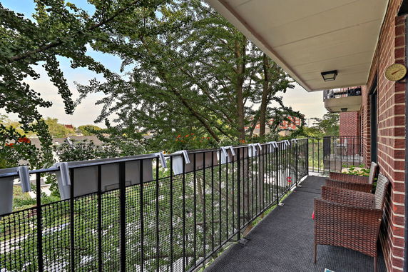 Balcony view overlooking trees and surrounding area with chairs and railing.