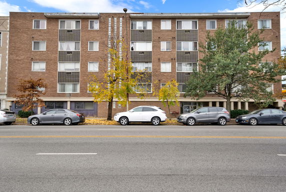 Front view of a multi-story brick building with parked cars in front.