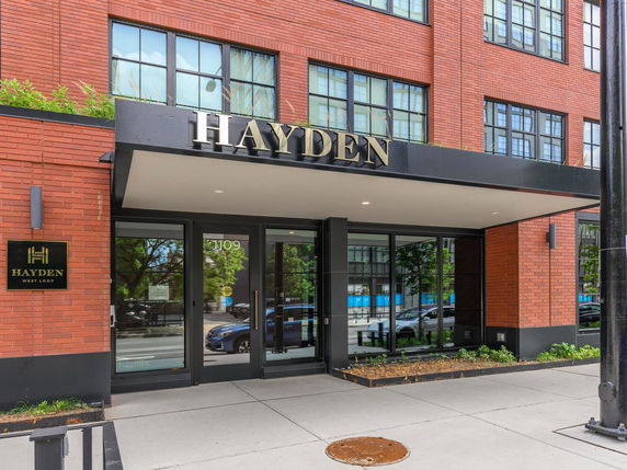 Front view of a multistory brick building entrance with large windows and signage above.