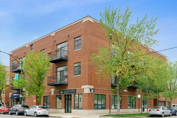 Front view of a three-story brick building with balconies and commercial spaces on the ground floor.