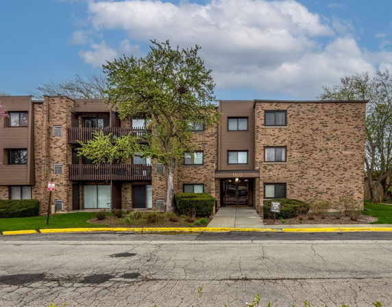 Front view of a three-story brick apartment building with balconies.