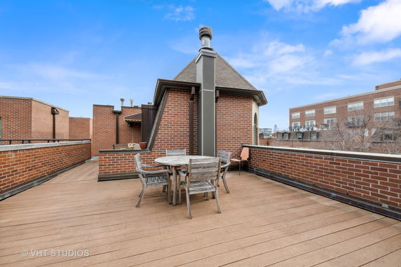 Rooftop view with brick walls, wooden deck, and small seating area.
