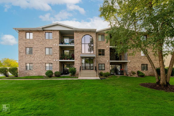 Front view of a three-story brick apartment building with a central entrance and balconies.