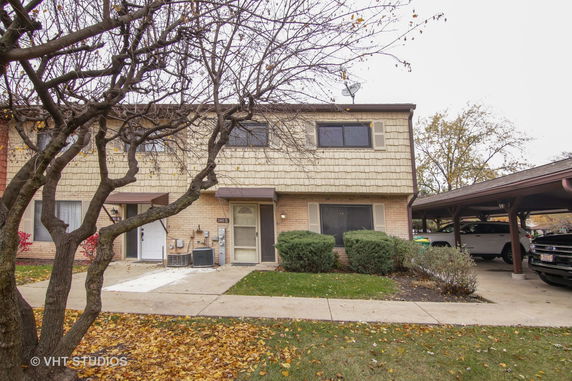 Front view of a two-story house with a brick facade and a covered parking area.