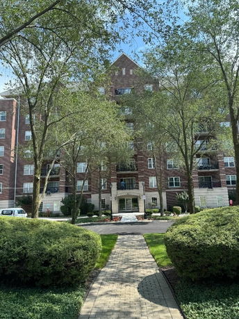 Front view of a multi-story brick residential building with balconies and greenery in the foreground.