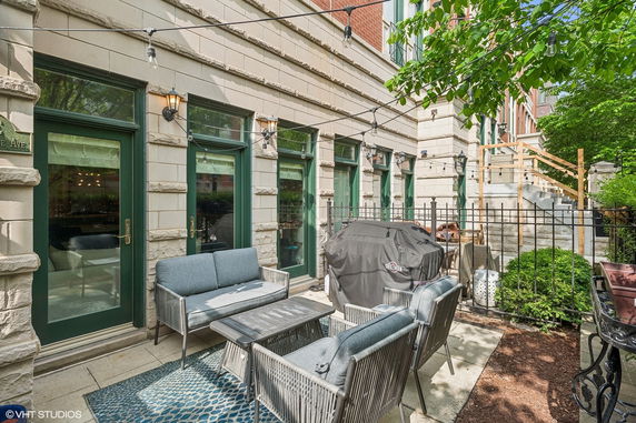 Outdoor seating area with patio furniture and grill in front of a building with green doors.
