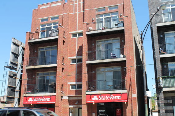 Front view of a multi-story brick building with balconies and a State Farm office on the ground floor.