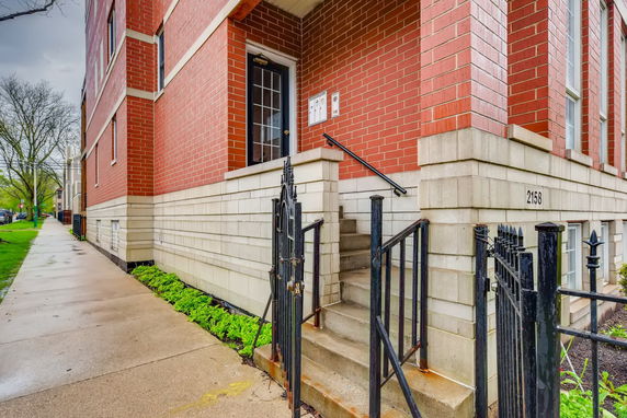 Front view of a brick building with stairs and a black metal gate entrance.